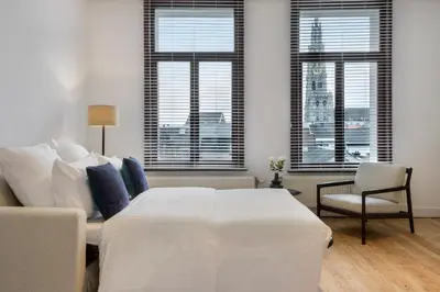 a bedroom with a bed and a couch and windows at The 1894 Boutique Holiday Apartment in Antwerp