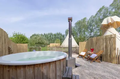 a hot tub in a backyard with an umbrella at Tipi Marie met hotutub in de tuin in Kaprijke