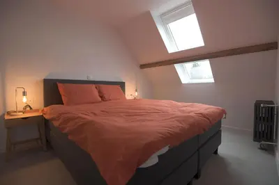 a bedroom with a bed with orange sheets and a table at Vakantiehuis huYze-K in Zottegem